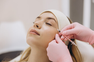 Cosmetologist making rejuvenating injection for wrinkles smoothing on face of female patient lying...
