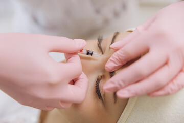 Cosmetologist wearing pink gloves injecting botox into female patient's forehead using a syringe