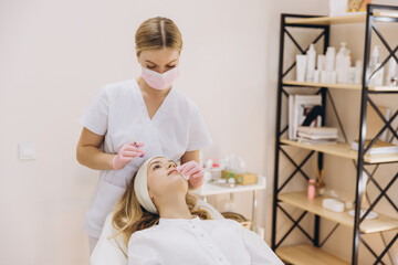 Beautician performing botox injection on forehead of young woman for rejuvenating facial treatment in beauty salon