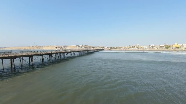 Rustic wooden pier extends over calm blue waters, leading to a vibrant coastal town. Ideal for travel blogs, wall art, or promotional content.