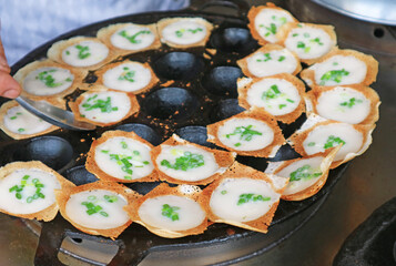 vendor taking Kanom Krok, popular Thai coconut milk pancake out from the pan when ready to serve