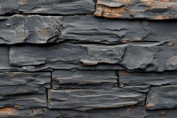 Obraz premium Textured black stone wall featuring layered rock formations with natural weathering markings