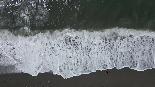Waves breaking on the volcanic beach. People walking next to waves. Aerial view from above. Coastline. Canary Islands. Spain.