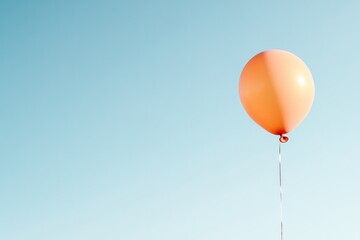 Obraz premium Bright orange balloon floats against clear blue sky, evoking joy