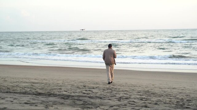 Close up male traveler controlling a drone using the remote control as it flies over the sunrise sea in the early hours of the morning. Man pilot with remote controller outdoors in nature at seascap