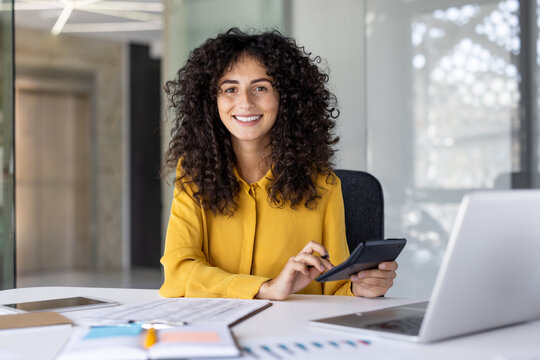 Successful financier accountant at workplace inside office. Businesswoman behind paperwork smiling and looking at camera. Satisfied female office worker, with graphs and charts.
