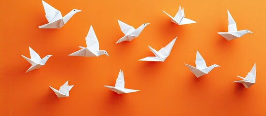 White origami birds scattered on vibrant orange background creating a dynamic flat lay arrangement highlighting elegance and simplicity