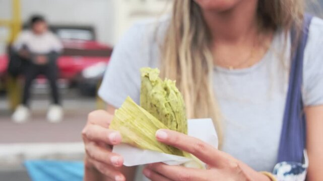 Close-up of young hispanic woman eating street food green tamale, Peruvian street food.