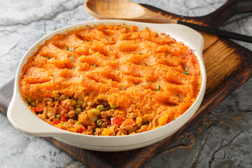 Sweet potato shepherd's pie with ground turkey, green peas, onions, peppers and tomatoes close-up in a baking dish on a wooden board. Horizontal