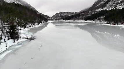 Drone view of melt water covers the ice on lake Haugavatnet with snowy mountains and misty sky