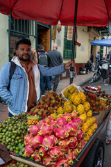 A male street vendor of likely Latin American descent displays a vibrant array of tropical fruits...
