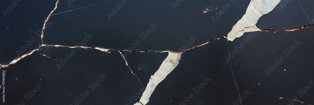 Poster texture of a black wall displaying cracks in plaster and light grey surfaces over time