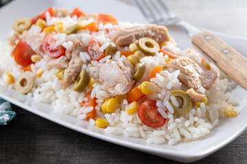 Rice salad with tomato, corn,olives and tuna on wooden table. Close up