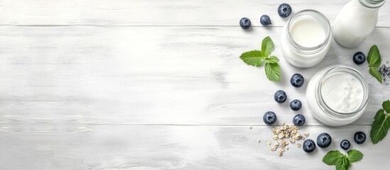 Healthy breakfast scene featuring homemade granola in a glass jar with yogurt, fresh blueberries, and mint leaves on a light wooden background.