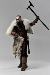 Obraz premium Viking warrior dressed in fur cloak and leather armor, raising battle axe with fierce expression, prepared for combat. Concept of Nordic warrior, medieval history, Norse mythology. Full-length
