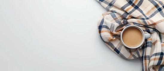 Cozy flat lay of a plaid scarf with warm tones and a cup of coffee on a bright white desk evoking an autumn Hygge atmosphere