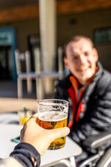 Hand holding a glass of beer with a blurred disabled man in a wheelchair