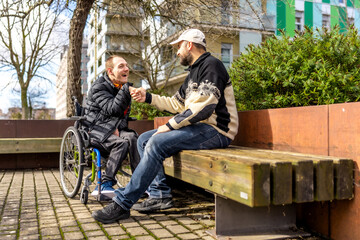 Disabled man in wheelchair shaking hands with friend on city bench