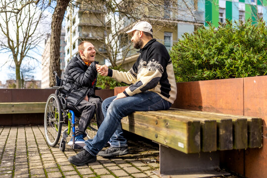 Disabled man in wheelchair shaking hands with friend on city bench