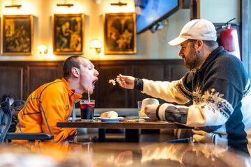 Caregiver feeding disabled man in restaurant, sharing a meal and promoting inclusion