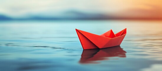Red paper ship leading among white paper ships on calm water at sunset with soft focus background highlighting leadership and teamwork concepts.