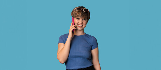 A Caucasian young woman is talking emotionally on a mobile phone on a blue background. Panoramic banner. A place for your text. Technology concept