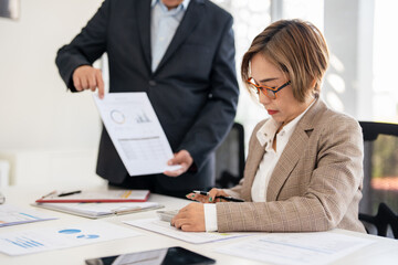 Fototapeta premium Senior professionals work on project in modern office, analyzing documents and charts. The man focuses intently the woman reviews papers with calculator ,dynamic scene of collaboration and expertise.