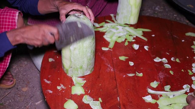 The man hand peeling wax gourd with the knife on the wooden table for the cooking.