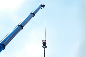 Blue crane arm, boom with hanging hook against clear sky. Construction and lifting heavy building...