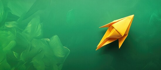 Handmade origami yellow paper rocket positioned on the right against a smooth green background with ample space for text insertion