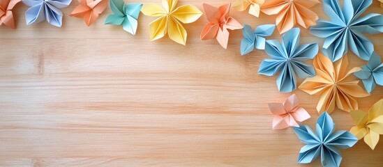 Colorful origami flowers in orange blue and yellow arranged on a light wooden desk creating a vibrant and artistic flat lay composition