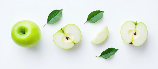 Fresh green apple with two halves and slices arranged artfully on a light background alongside green leaves top view.