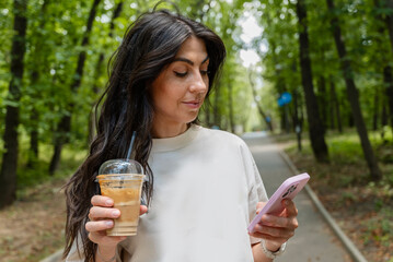 Woman walking in the summer park ,drinking coffee ,looking  her phone