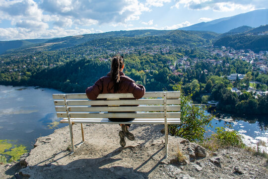 Traveler woman sitting on a bench high above a blue lake with stunning panoramic view 