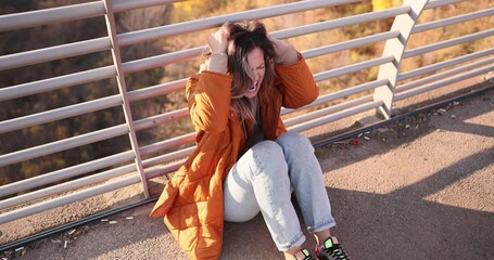 Emotional young woman experiences intense mental distress sitting near metal railing. Lady with overwhelming feelings of sadness grief and anxiety