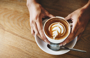 Hands, latte art and wooden table with customer in coffee shop for hospitality, relax or service. Artistic, beverage and cup with person in cafe or restaurant for morning caffeine drink from above