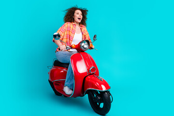 Joyful young woman riding a red scooter with a teal background showcasing lifestyle and happiness