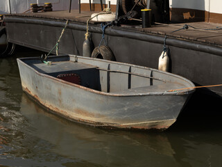 Small metal boat moored to a dock, showing signs of wear and rust. Urban riverside scene, simple watercraft, utilitarian design © Maciej Bonk