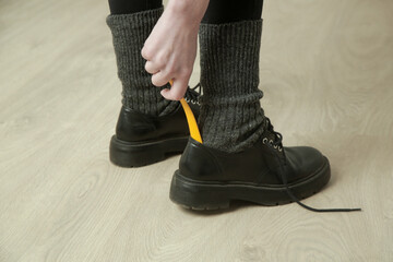 Woman is putting on shoes using yellow plastic shoehorn.