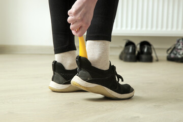 Woman is putting on shoes using yellow plastic shoehorn.