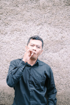 Man in black contemplates with cigarette against a textured wall