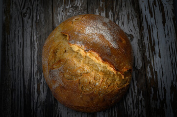 Freshly baked round loaf resting on rustic wooden table with a golden crust and floury texture