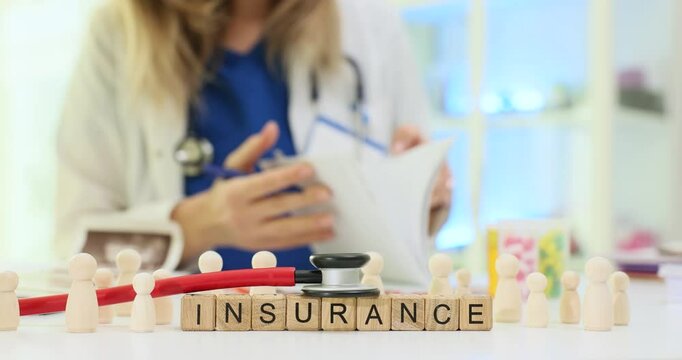Word Insurance with wooden figures showing people and stethoscope on doctor table. Therapist checks patient agreement sitting at desk in clinic setting
