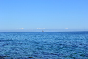 a small white sail boat went out to sea on a clear sunny day
