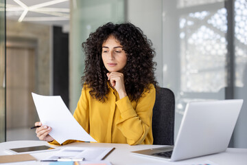 Serious focused thinking woman behind paperwork. Businesswoman reading report calmly and thoughtfully, working with contracts and papers documents inside office at workplace.