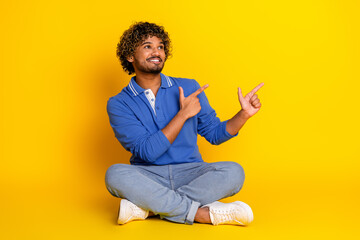 Young stylish man sitting casually on a yellow background pointing with both hands, joyful and...