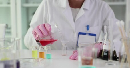 Scientific worker pours red chemical solution into flask at desk. Technician conducts research experiment in sterile laboratory environment - Powered by Adobe