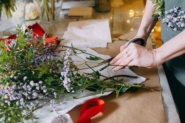 A florist works on preparing beautiful floral arrangement. Various flowers and materials lie on table, emphasizing the artistic and inspiring atmosphere associated with floral design and presentation.