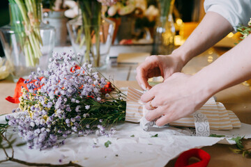 A florist works on preparing beautiful floral arrangement. Various flowers and materials lie on table, emphasizing the artistic and inspiring atmosphere associated with floral design and presentation.