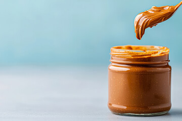 Creamy caramel spread in glass jar against blue background